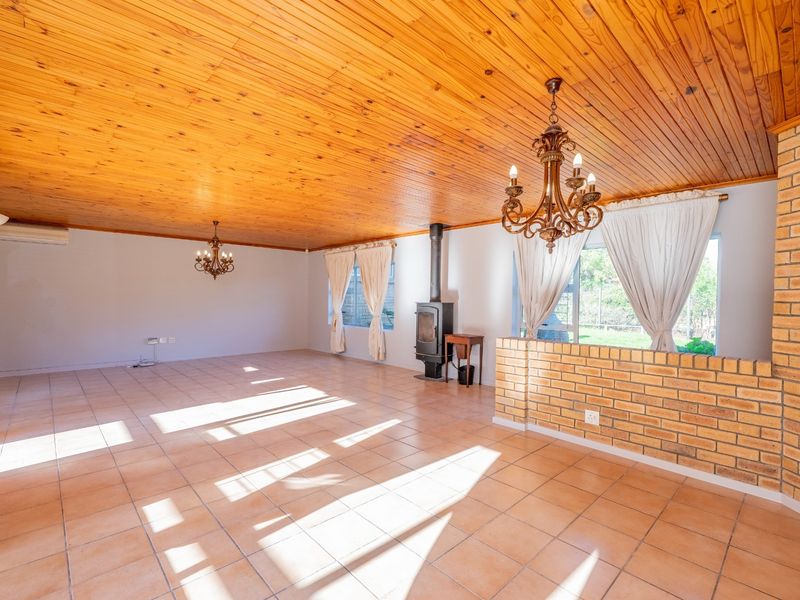 Spacious living area featuring a warm wood-paneled ceiling, tiled floors, a brick feature wall, and a built-in freestanding fireplace.