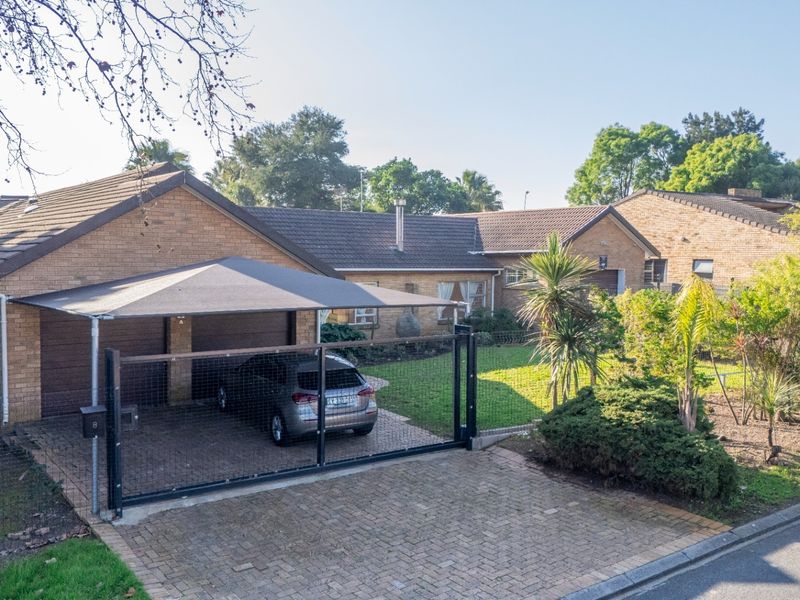 Front view of a brick house featuring a double garage, shade cloth carport, paved driveway, and a secure fenced garden area.