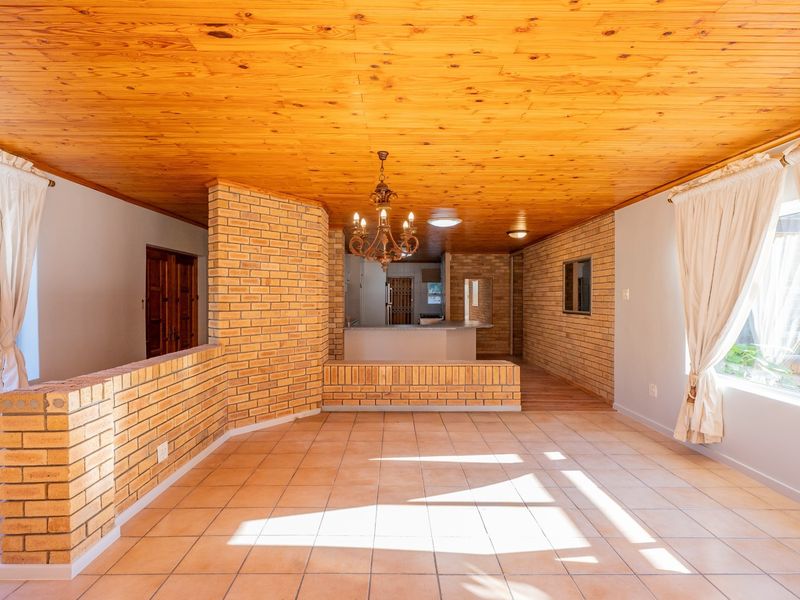 Spacious open-plan living area featuring exposed brick walls, a warm timber ceiling, and neutral ceramic floor tiles, offering a versatile layout for modern living.