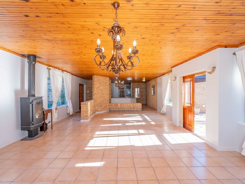 Spacious open-plan living area featuring a wood-burning fireplace, timber ceiling, and tiled flooring, with direct access to the outdoor patio area.