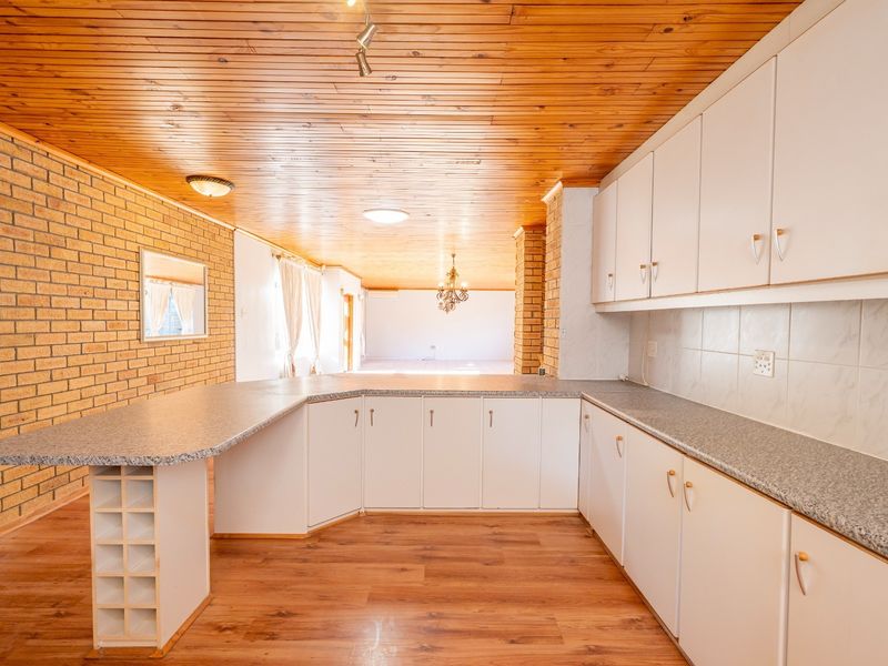 Spacious open-plan kitchen featuring timber ceilings, exposed brick walls, and ample built-in cabinetry with laminate countertops.