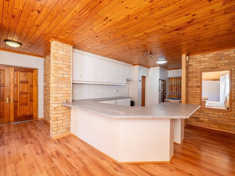 Spacious kitchen featuring exposed brick pillars, timber ceiling, laminate countertops, and ample built-in cabinetry in an open-plan layout.