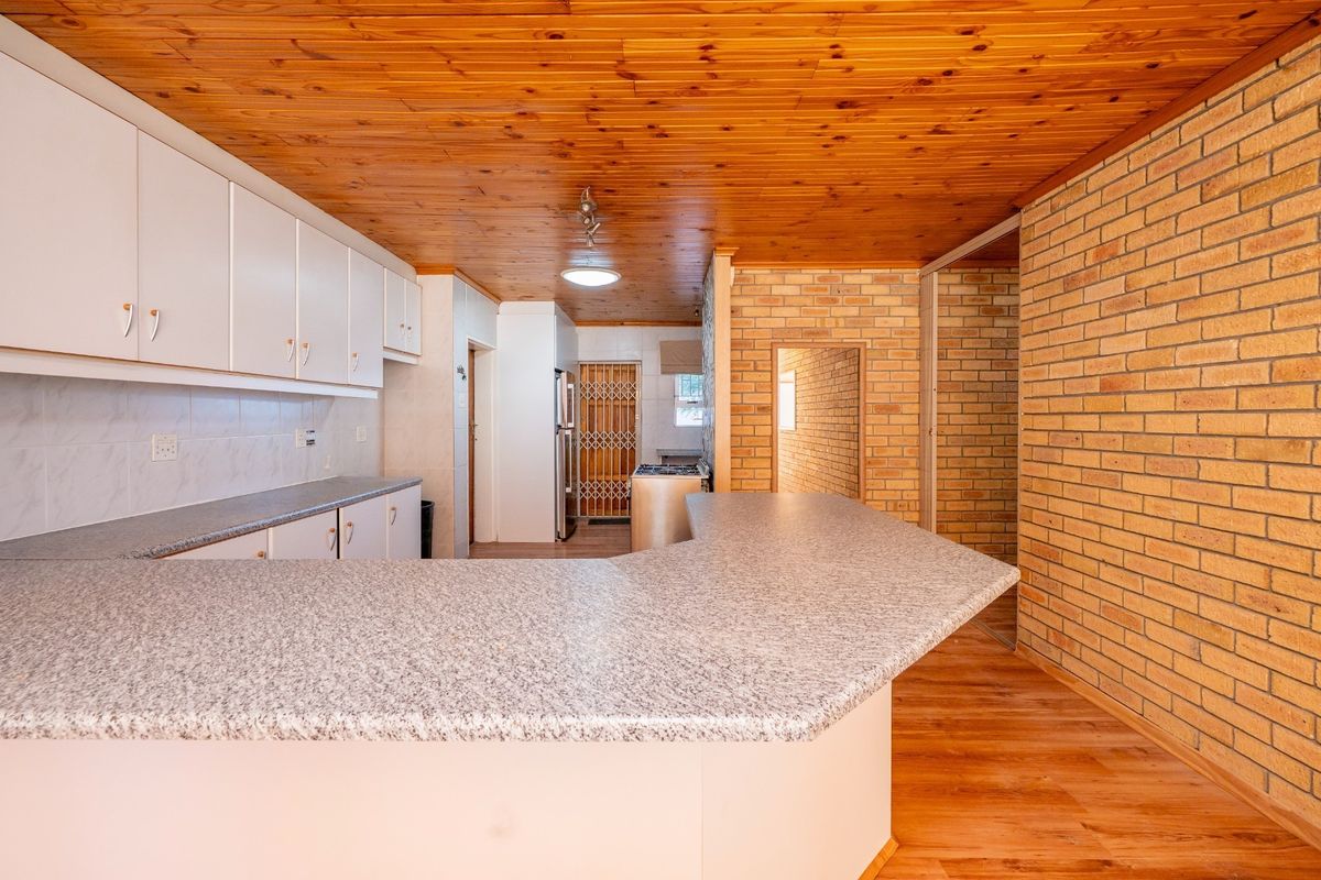 A functional kitchen featuring laminate countertops, built-in cabinetry, exposed brick walls, and a timber ceiling, offering a classic, dated aesthetic ready for modernization.