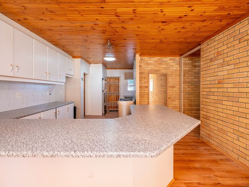 A functional kitchen featuring laminate countertops, built-in cabinetry, exposed brick walls, and a timber ceiling, offering a classic, dated aesthetic ready for modernization.