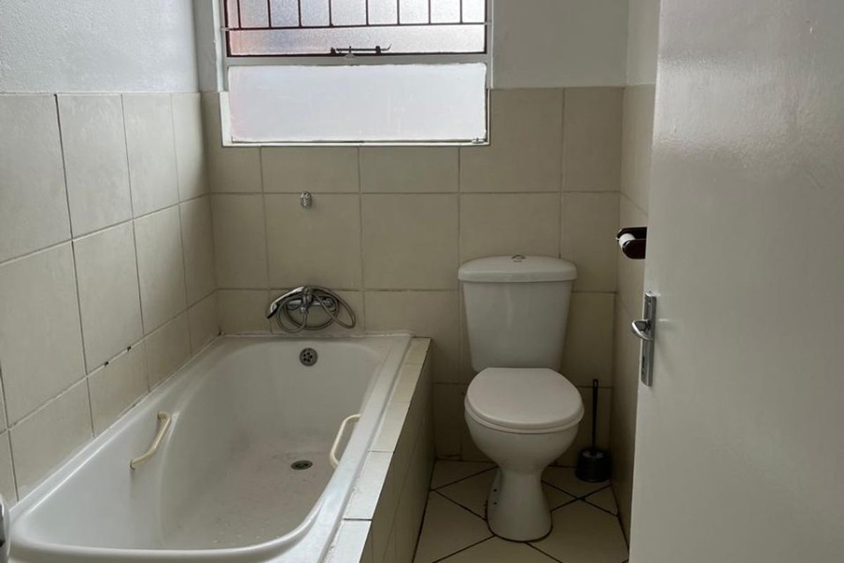 A functional bathroom featuring a built-in bathtub, toilet, and tiled finishes, requiring cosmetic updates to improve its overall condition and appeal.