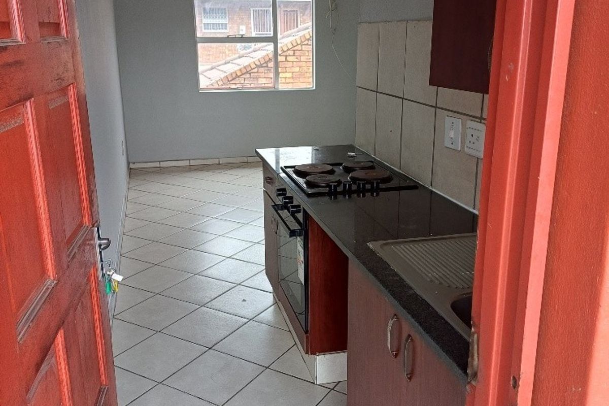 A compact kitchen featuring built-in cabinetry, a dark countertop, an integrated electric hob and oven, and tiled flooring.