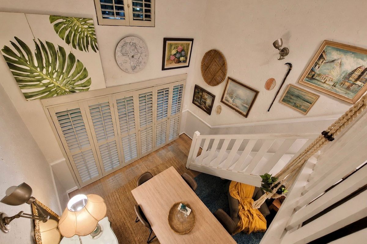 A high-angle view of a living area featuring a staircase with a white balustrade, plantation shutters, and wall-mounted lighting fixtures.