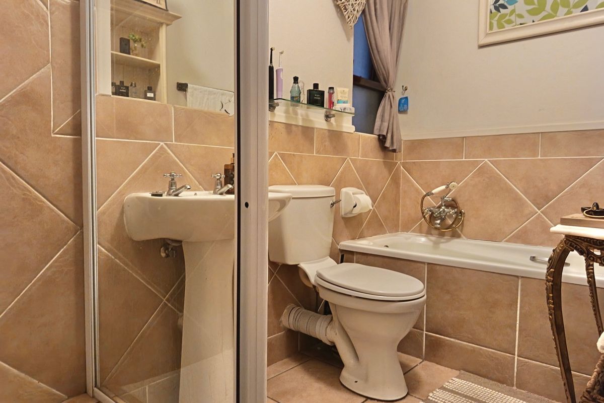 A functional bathroom featuring a pedestal basin, toilet, and bathtub with neutral wall and floor tiling.