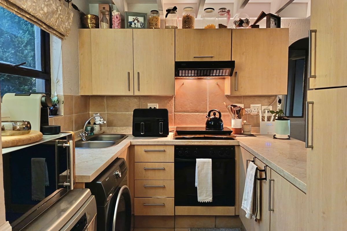 Compact kitchen featuring light wood cabinetry, laminate countertops, built-in oven with extractor fan, and tiled backsplash with exposed ceiling beams.