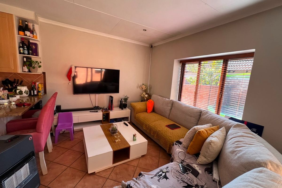 A comfortable living room featuring terracotta floor tiles, built-in shelving, and large windows with venetian blinds, providing a functional and inviting space.