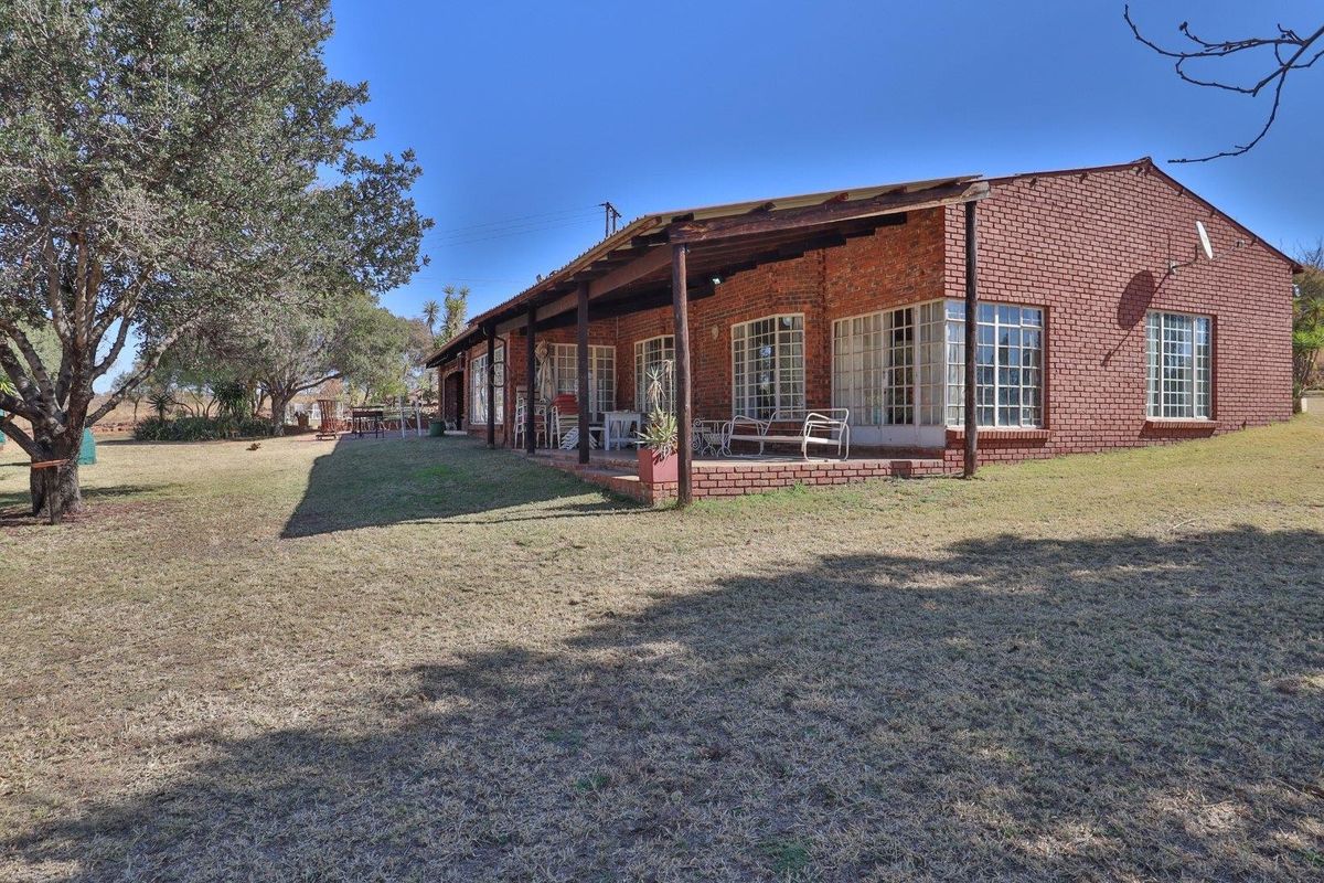 Rear view of a farm-style residence featuring an exposed brick facade and a covered timber patio overlooking a large garden area.