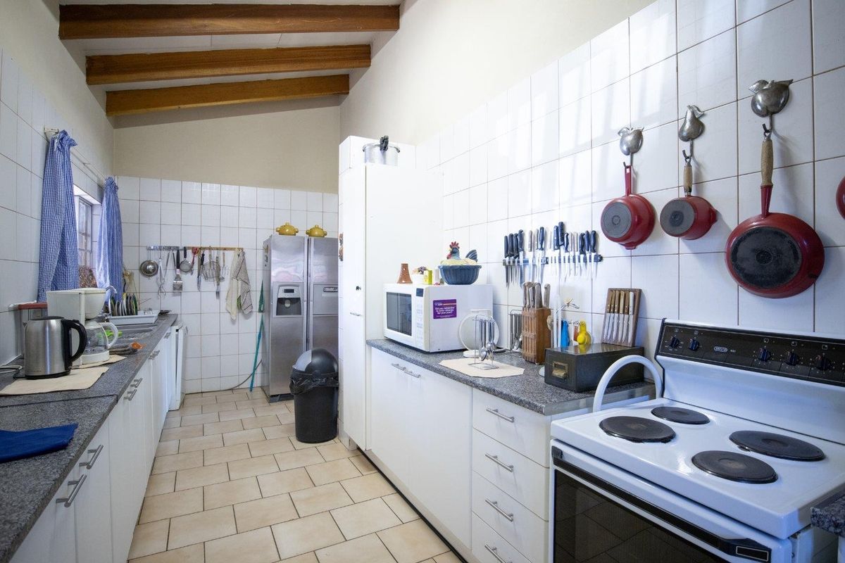 A functional kitchen featuring exposed timber ceiling beams, granite countertops, tiled splashbacks, and ample built-in cabinetry with a freestanding electric stove.