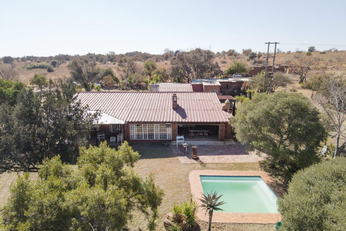 Aerial view of a farm property featuring a brick residence with a metal roof, a covered patio area, and an outdoor swimming pool.