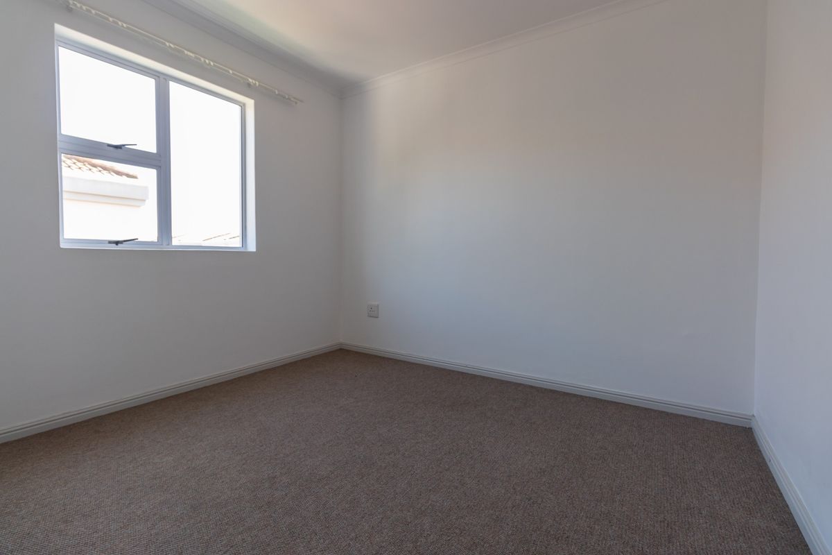 A clean, empty bedroom featuring neutral carpeted flooring, white walls, and a window providing natural light.