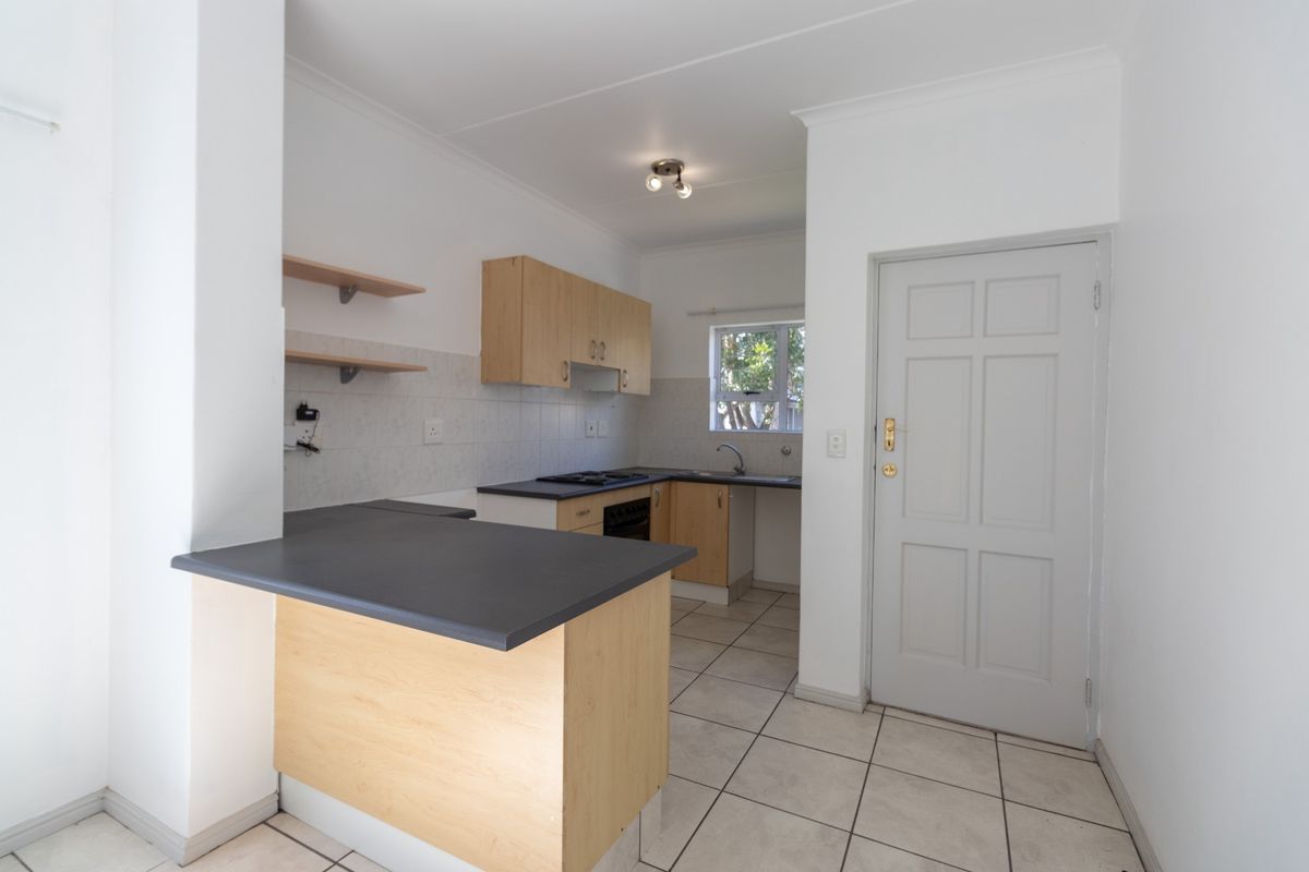 A functional kitchen featuring light wood cabinetry, dark laminate countertops, built-in oven and hob, and tiled flooring, offering a clean and practical workspace.