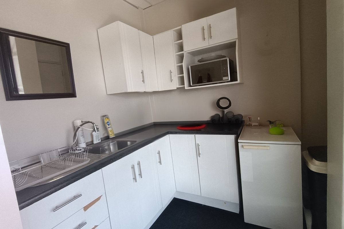 A compact office kitchenette featuring white cabinetry, dark laminate countertops, a stainless steel sink, and a built-in microwave.
