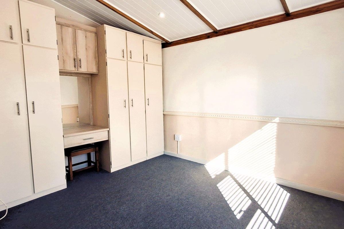 A bright, empty bedroom featuring built-in cupboards, a vanity station, carpeted flooring, and a timber-paneled ceiling.