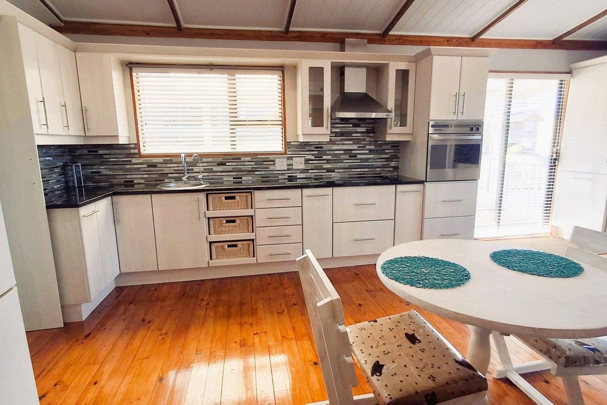 A well-maintained kitchen featuring timber flooring, built-in cabinetry, a tiled backsplash, and integrated appliances, with an adjacent dining area.