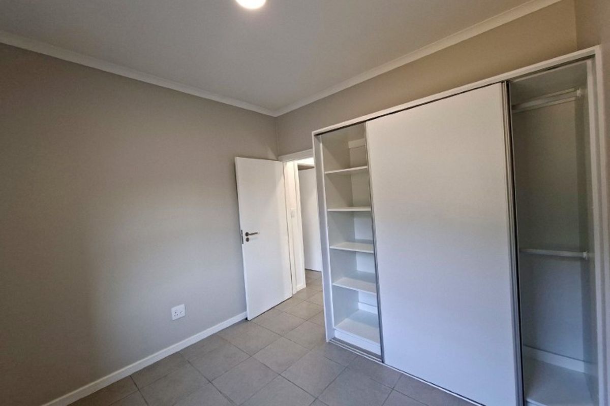 A clean, empty bedroom featuring neutral wall tones, tiled flooring, and a modern built-in sliding door wardrobe with integrated shelving.