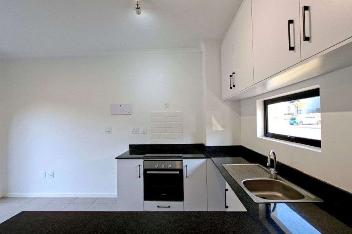 Modern kitchen featuring white cabinetry, dark granite countertops, built-in oven, electric hob, and a stainless steel sink with a tiled backsplash.
