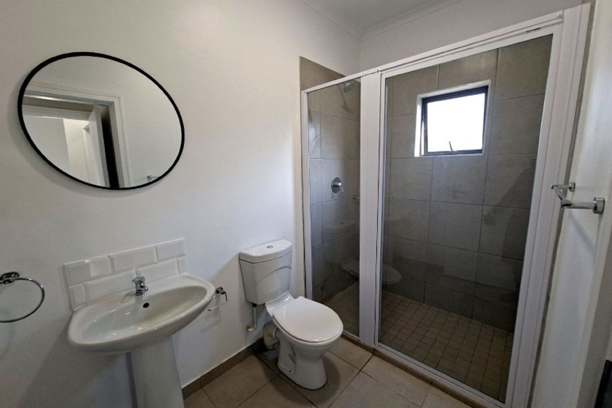 A clean and functional bathroom featuring a pedestal basin, toilet, and a glass-enclosed shower with neutral wall and floor tiling.