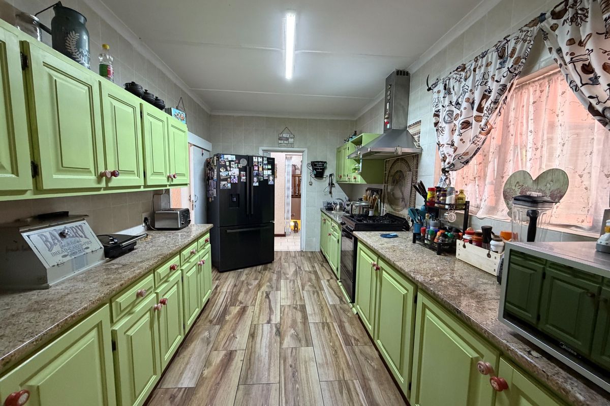 A functional galley-style kitchen featuring green cabinetry, granite countertops, wood-look laminate flooring, and a stainless steel extractor fan.