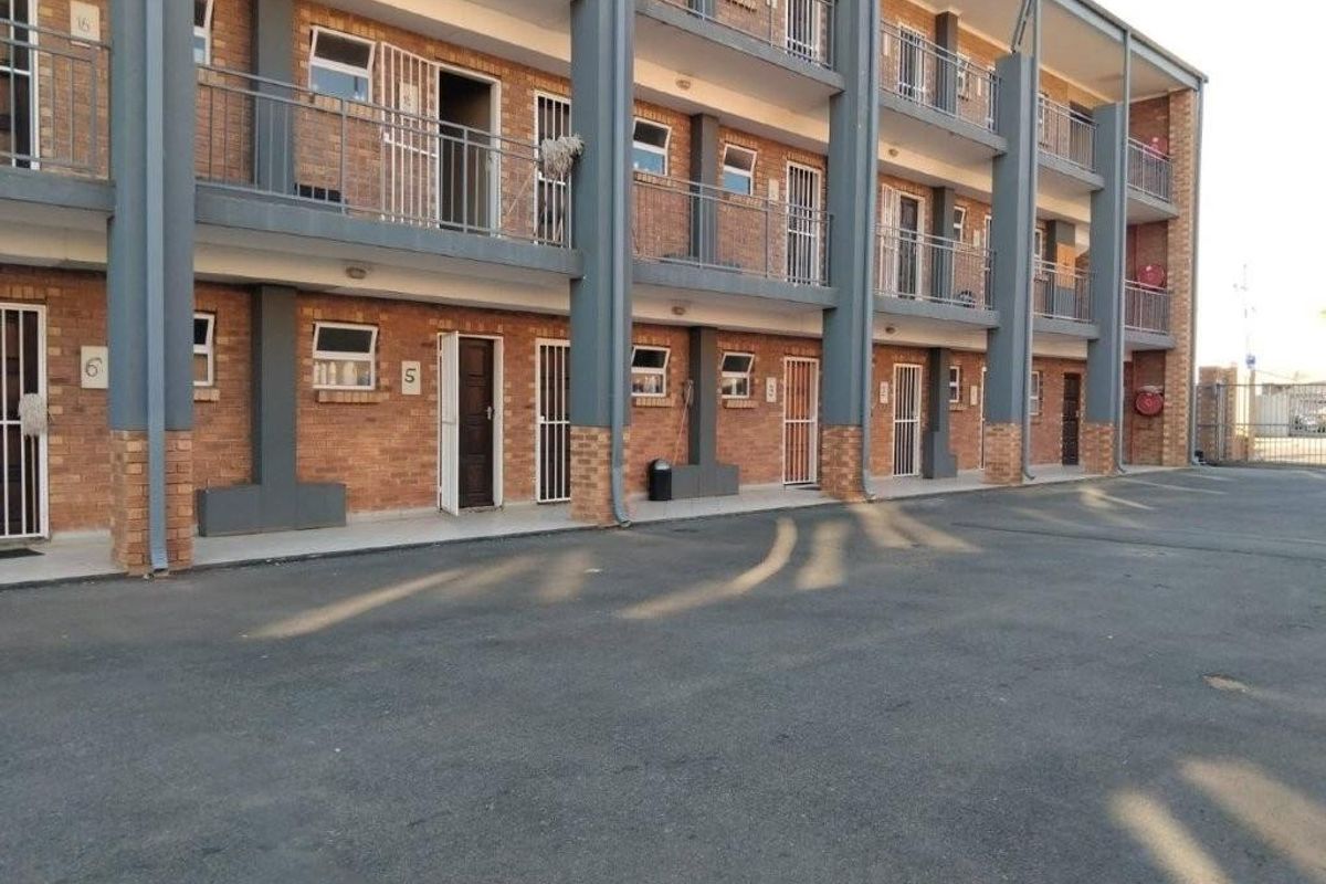 Exterior view of a multi-story apartment complex featuring brick facade, metal security gates, and balcony access for individual units.