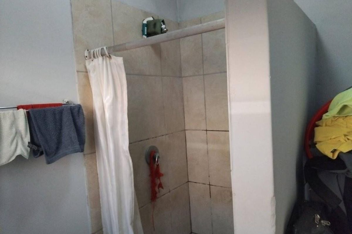 A functional bathroom shower area featuring tiled walls and a standard shower mixer, currently showing signs of wear and dated finishes.