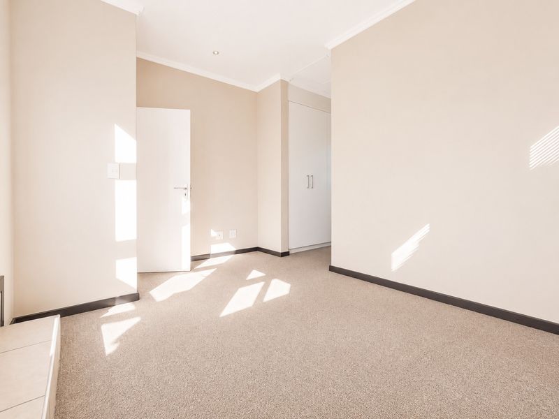 A bright, empty bedroom featuring neutral walls, carpeted flooring, and built-in cupboards, offering a clean and versatile space ready for personalization.