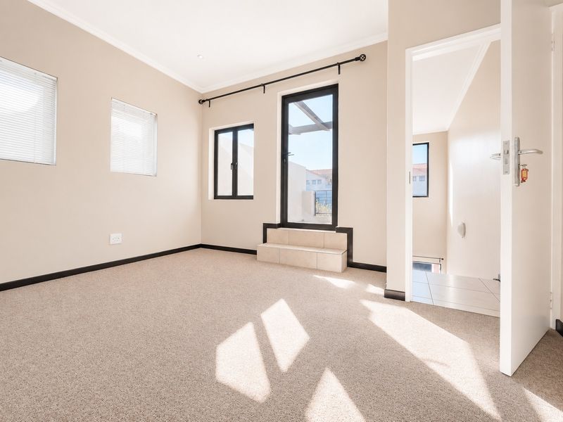 A bright, empty bedroom featuring neutral carpeting, aluminium window frames, and a tiled step leading to an exterior door.
