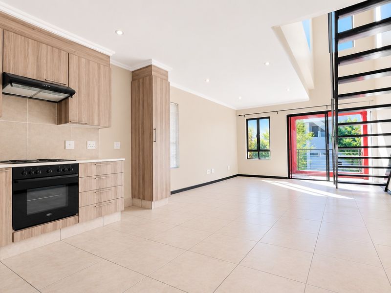 Spacious open-plan living area featuring a modern kitchen with built-in appliances, tiled flooring, and a striking metal staircase leading to the upper level.