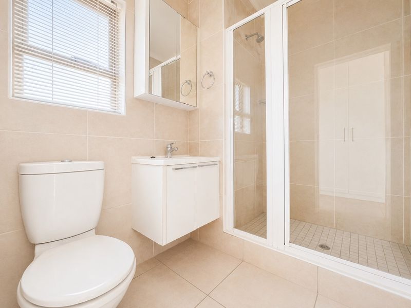 A clean, modern bathroom featuring a glass-enclosed shower, wall-mounted vanity, and neutral floor-to-ceiling tiling.