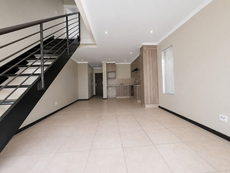 Spacious open-plan living and kitchen area featuring tiled flooring, modern built-in cabinetry, and a striking staircase with a metal balustrade.
