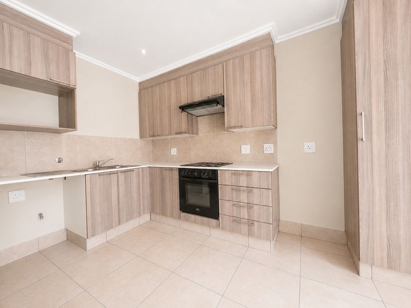 A clean, modern kitchen featuring light wood-grain cabinetry, built-in oven, gas hob, extractor fan, and neutral tiled flooring.