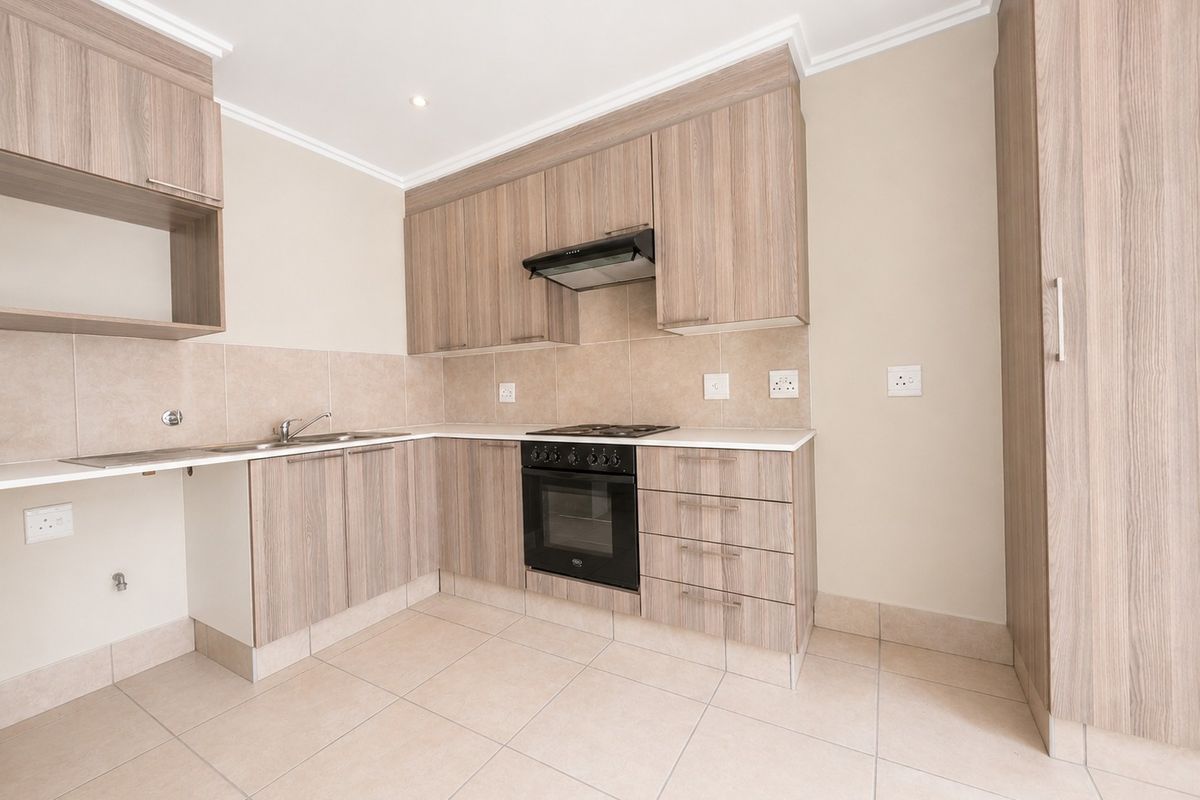 A clean, modern kitchen featuring light wood-grain cabinetry, built-in oven, gas hob, extractor fan, and neutral tiled flooring.