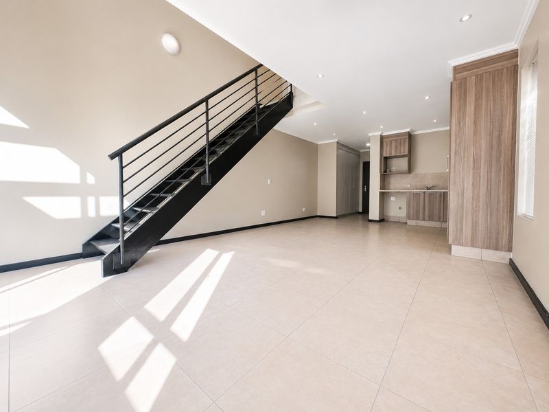 Spacious open-plan living area featuring modern tiled flooring, a sleek metal staircase, and a compact kitchen with built-in cabinetry.