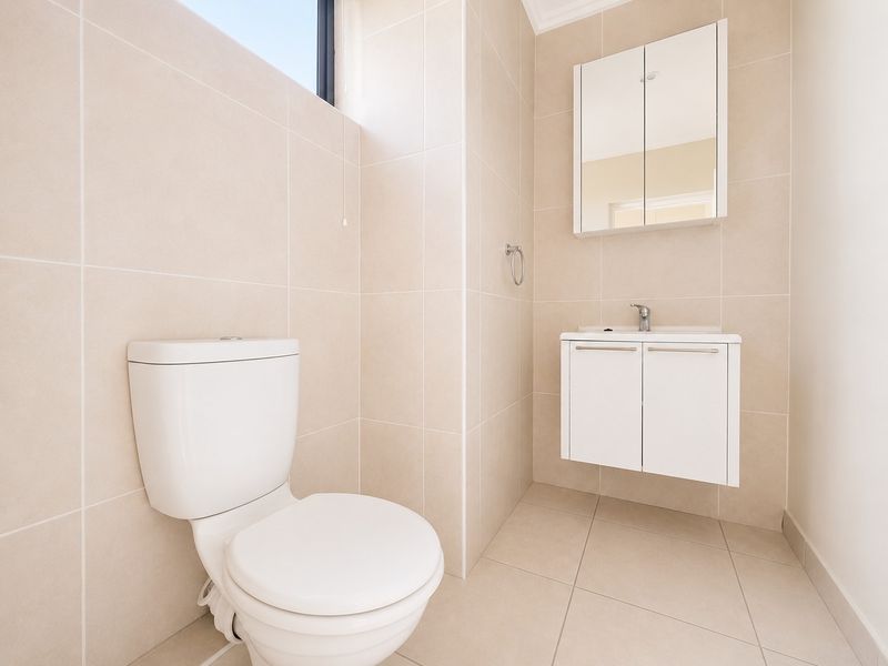 A clean, modern bathroom featuring neutral floor-to-ceiling tiling, a wall-mounted vanity with a basin, and a mirrored medicine cabinet.