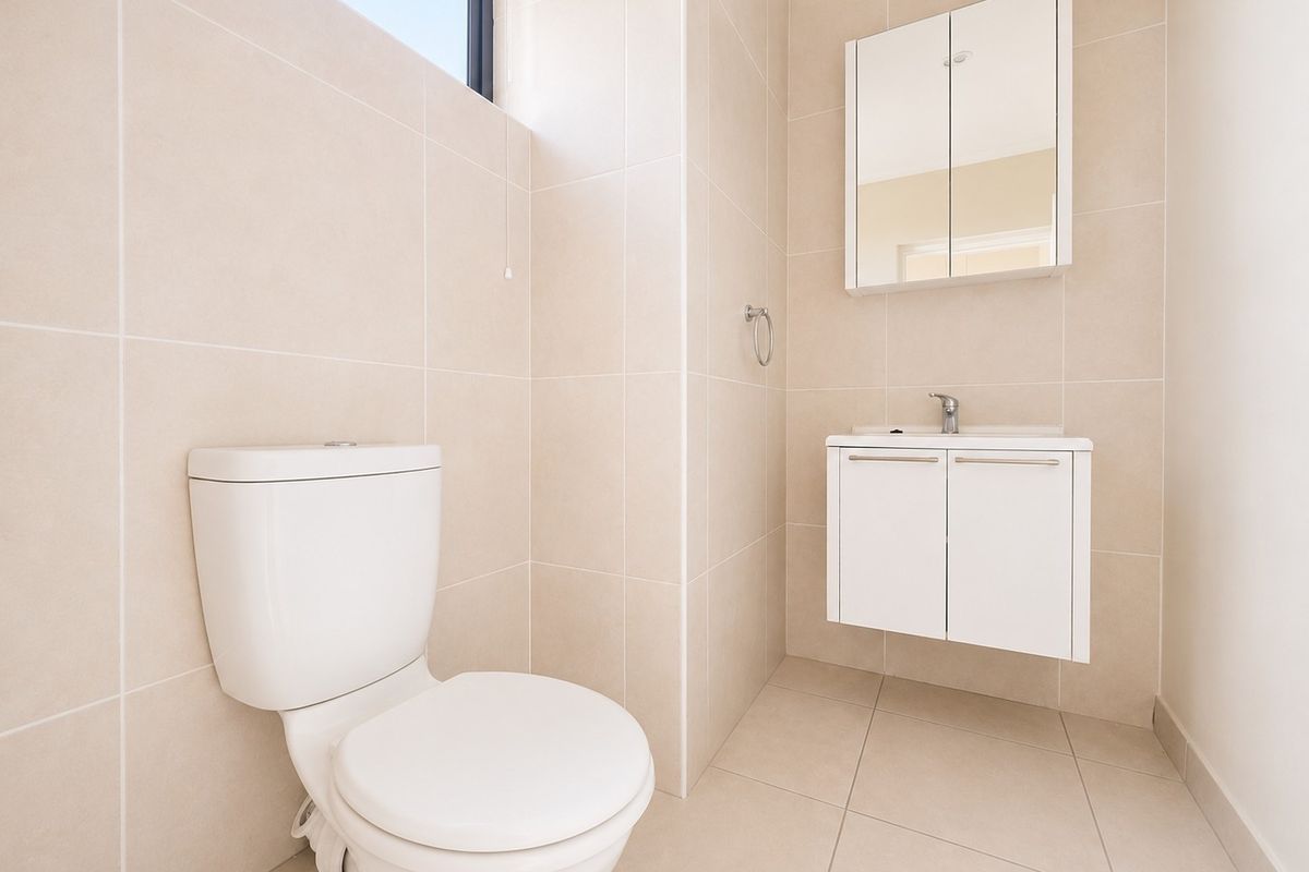 A clean, modern bathroom featuring neutral floor-to-ceiling tiling, a wall-mounted vanity with a basin, and a mirrored medicine cabinet.