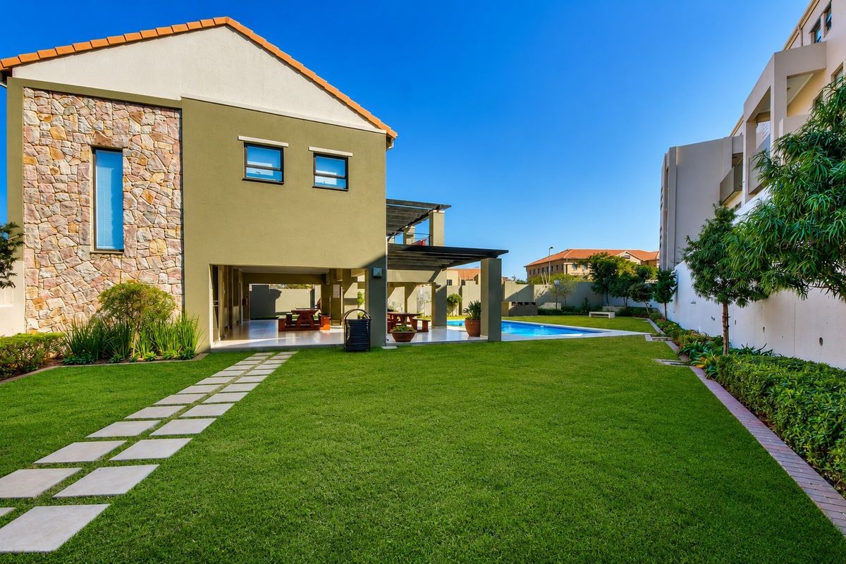 Spacious rear garden featuring a well-maintained lawn, a swimming pool, and a covered patio area with stone-clad exterior wall detailing.