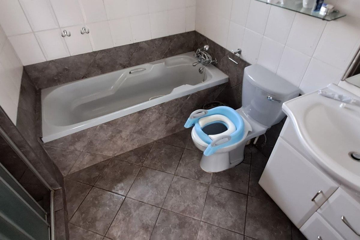 A functional bathroom featuring a built-in bathtub, a vanity with a washbasin, and a shower enclosure, finished with neutral wall and floor tiling.