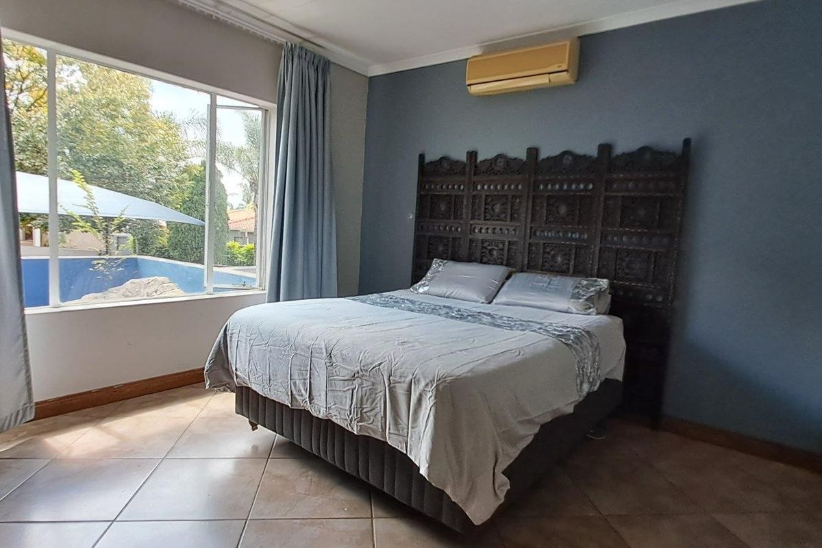 Spacious bedroom featuring tiled flooring, a wall-mounted air conditioning unit, and a large window overlooking the outdoor pool area.