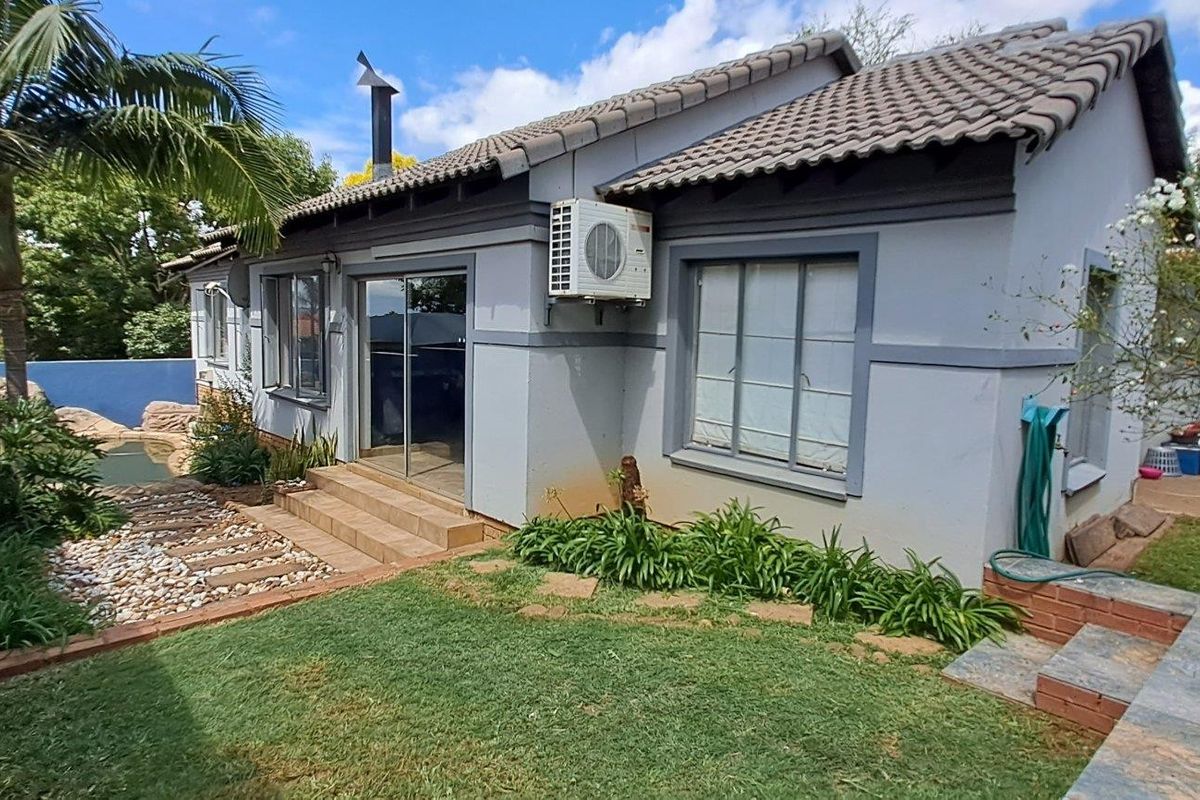 Rear view of the house featuring a tiled roof, sliding glass door access, an external air conditioning unit, and a landscaped garden area.