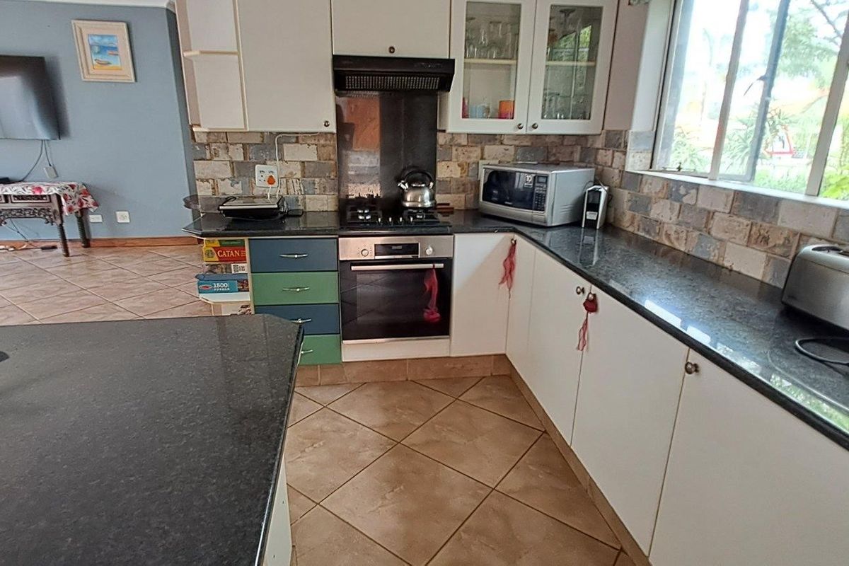 A functional kitchen featuring granite countertops, a gas hob with extractor fan, built-in oven, and stone tile backsplash, complemented by tiled flooring.