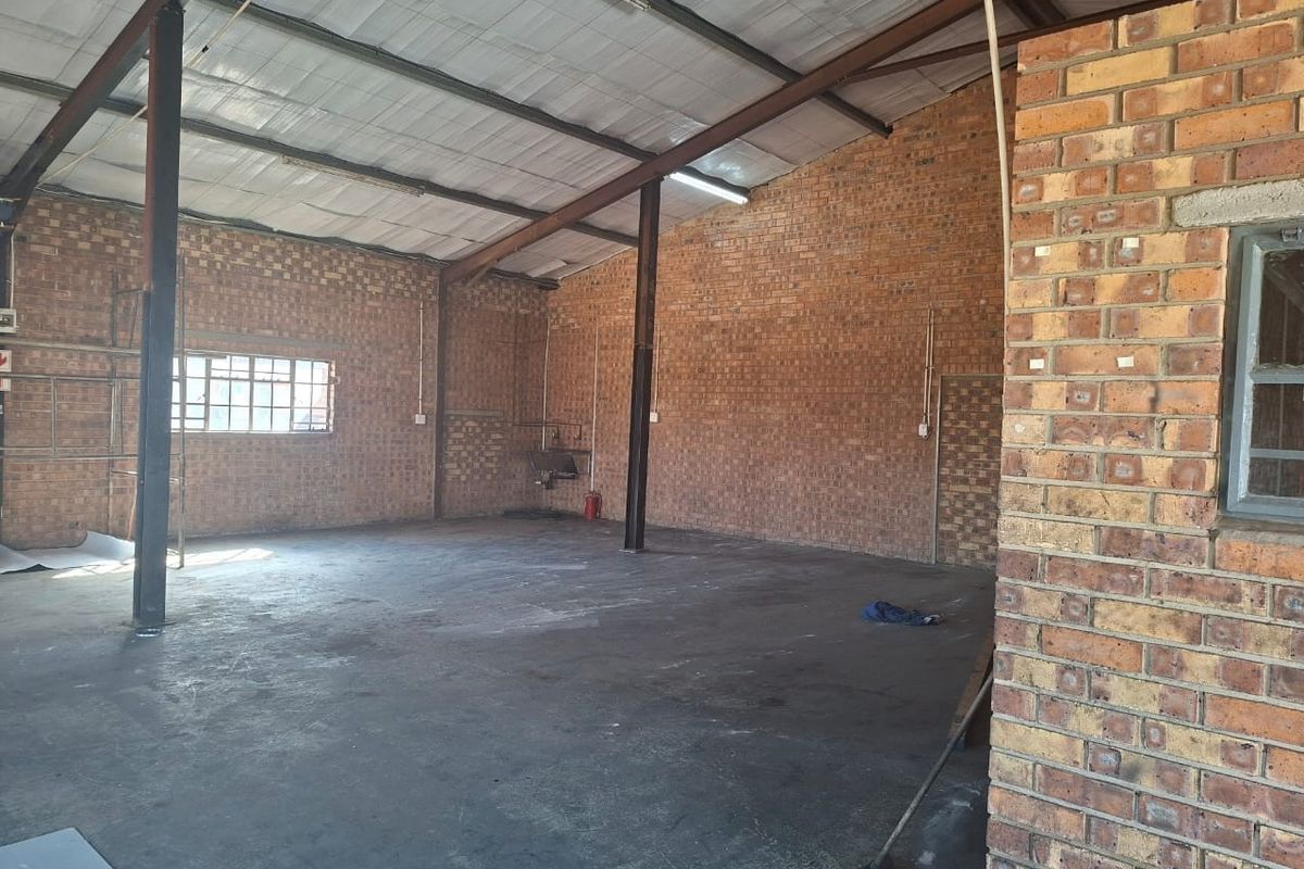 Spacious industrial utility area featuring exposed brick walls, concrete flooring, and high-pitched metal roofing with steel support structures.