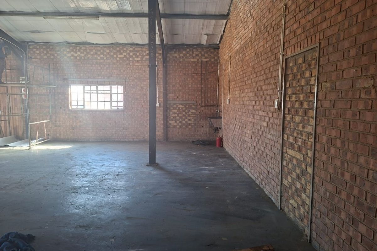 Spacious industrial utility area featuring exposed brick walls, concrete flooring, and a steel support column, suitable for workshop or storage use.