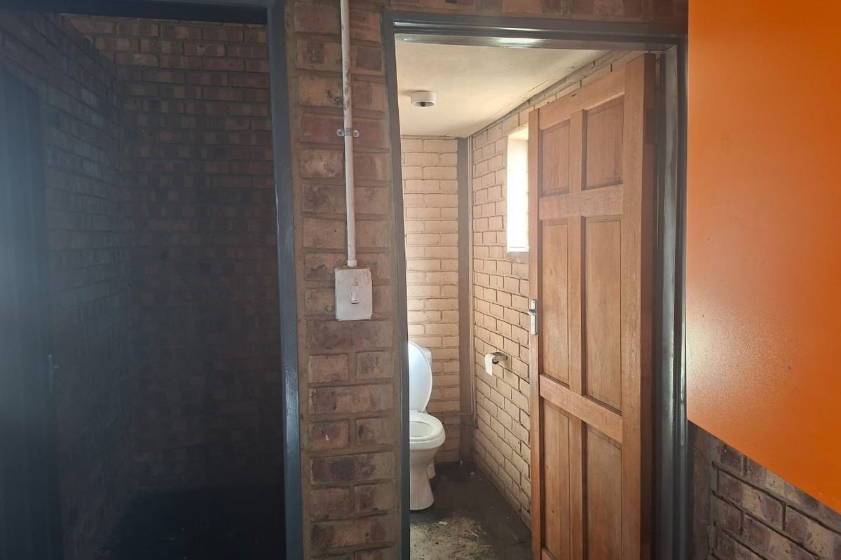 A functional bathroom space featuring exposed brick walls, a standard toilet, and a wooden door, requiring cosmetic updates to improve its overall condition.