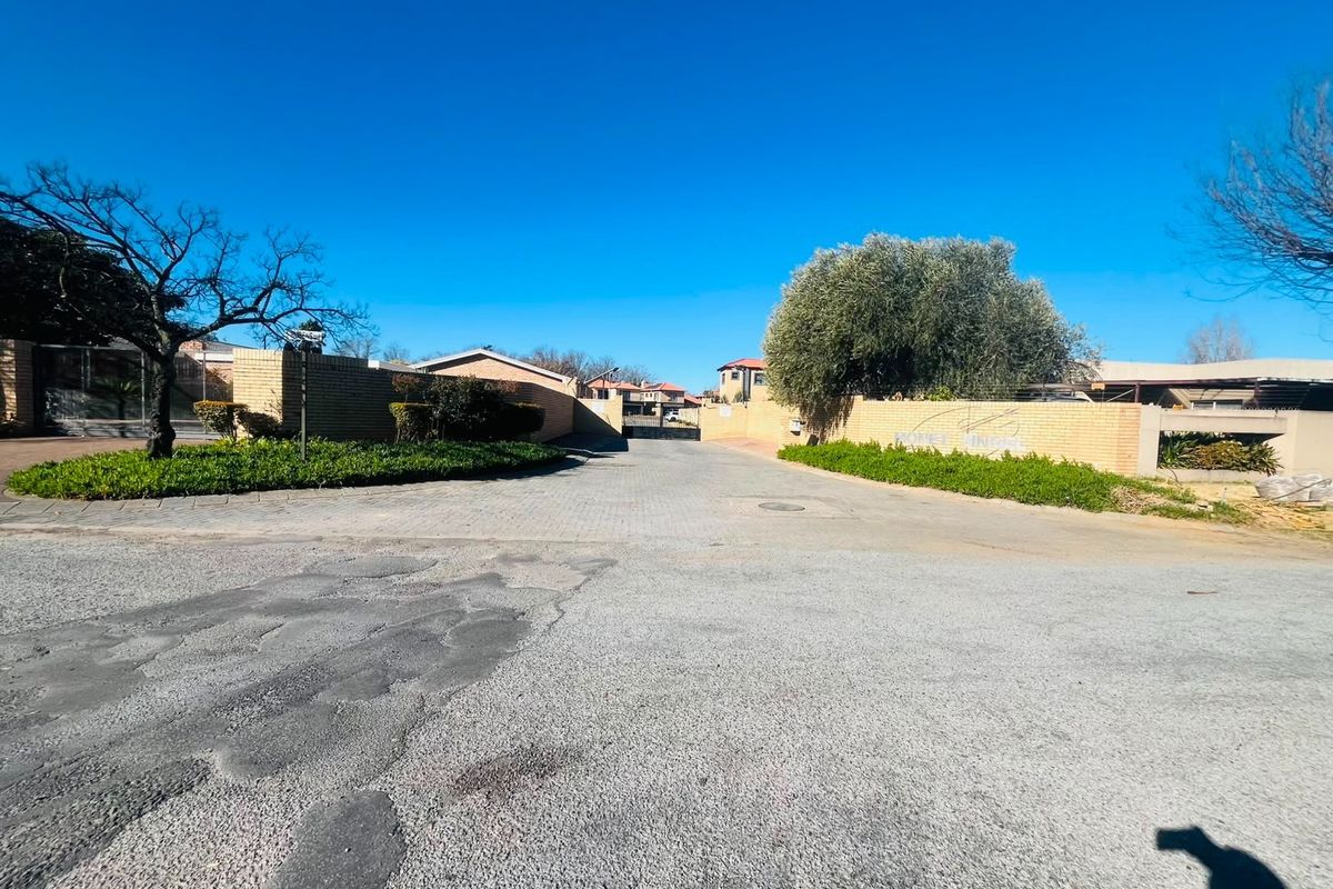 Street view of the residential property entrance featuring a paved driveway, brick boundary walls, and security gate access.
