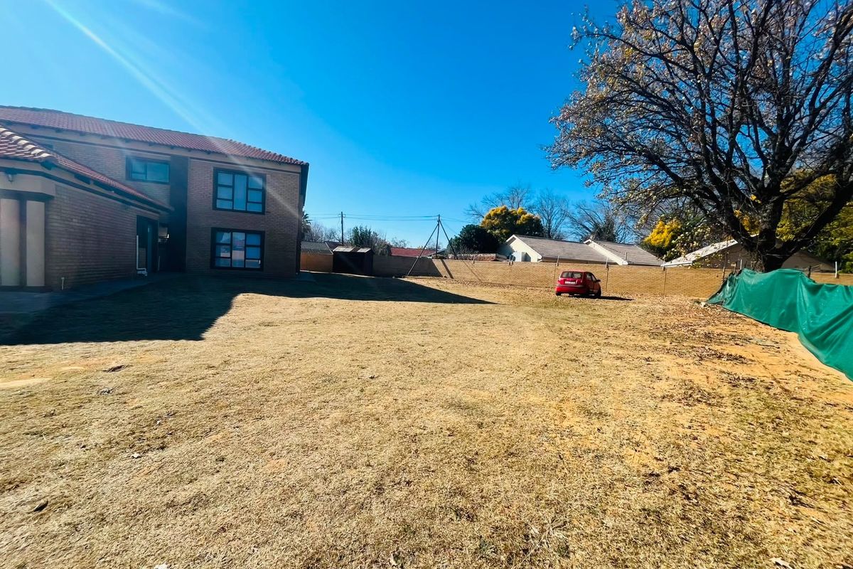 A spacious rear yard featuring a large lawn area, brick boundary wall, and a view of the adjacent residential building structure.