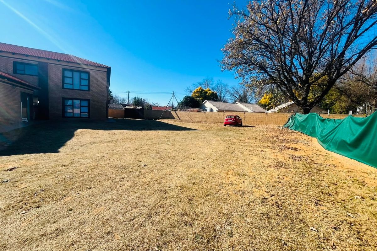 A spacious rear garden area featuring a large lawn, brick boundary walling, and a view of the adjacent residential building structure.