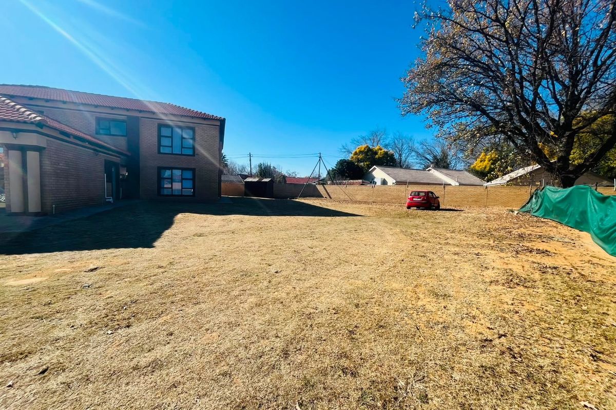 A spacious rear yard featuring a large lawn area, brick boundary wall, and a view of the rear elevation of the residential building.